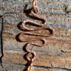 A squiggle of hammered copper wire; three translucent orange beads and an amber-colored one hang from the bottom.
