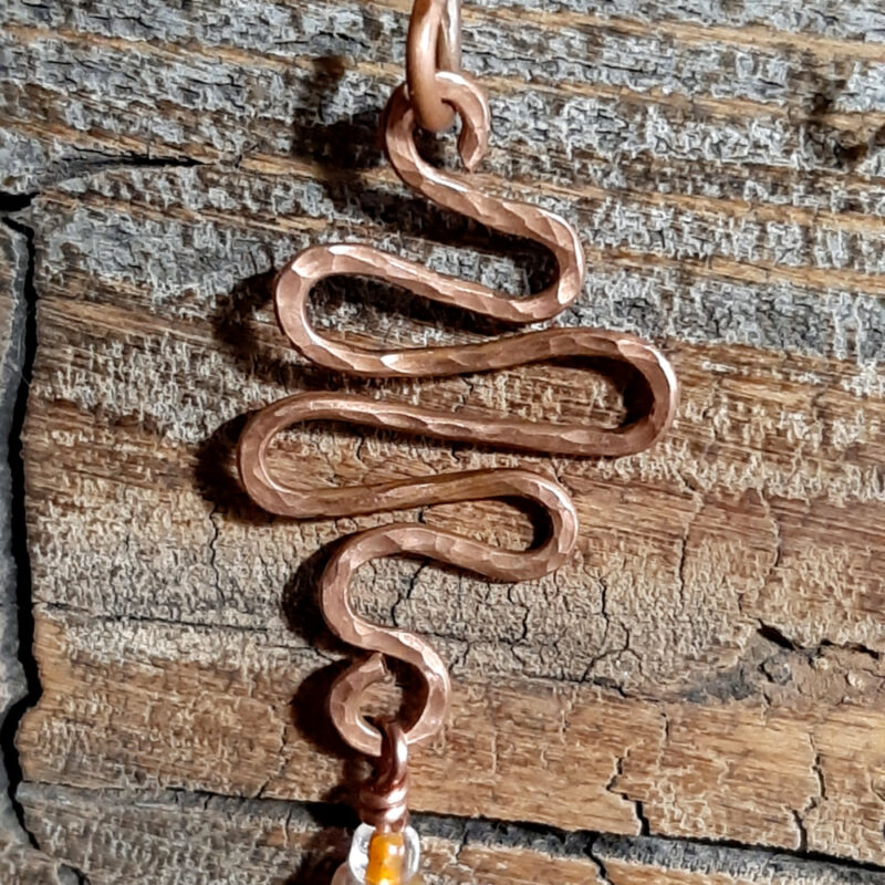 A squiggle of hammered copper wire; three translucent orange beads and an amber-colored one hang from the bottom.