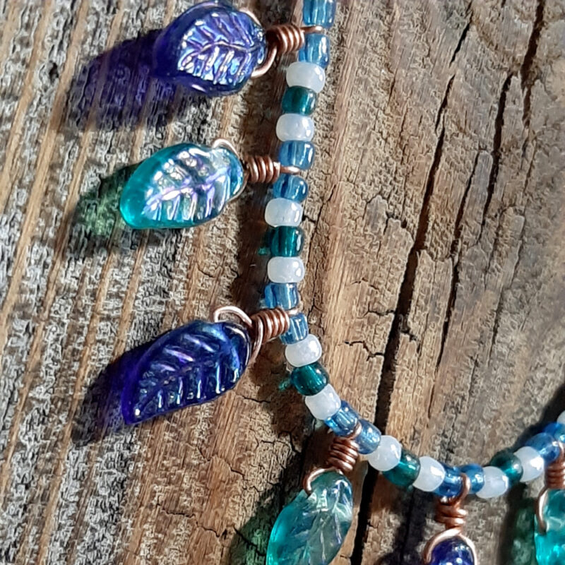 This necklace has small glass beads in blue, white, and green, with nine glass leaves, alternating green and blue, hanging along the front center.