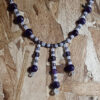 This necklace has alternating white and purple beads, with three short lengths of the same beads dangling from the center front.